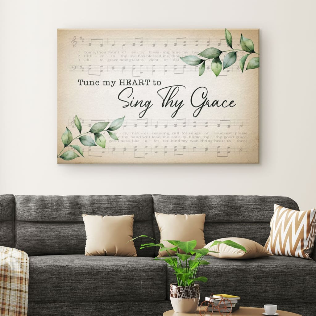 Christian wall art canvas with the phrase "Tune My Heart to Sing Thy Grace" overlaid on sheet music and green leaves.