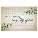 Inspirational wall art with "Tune My Heart to Sing Thy Grace," set against a backdrop of sheet music and lush green leaves.